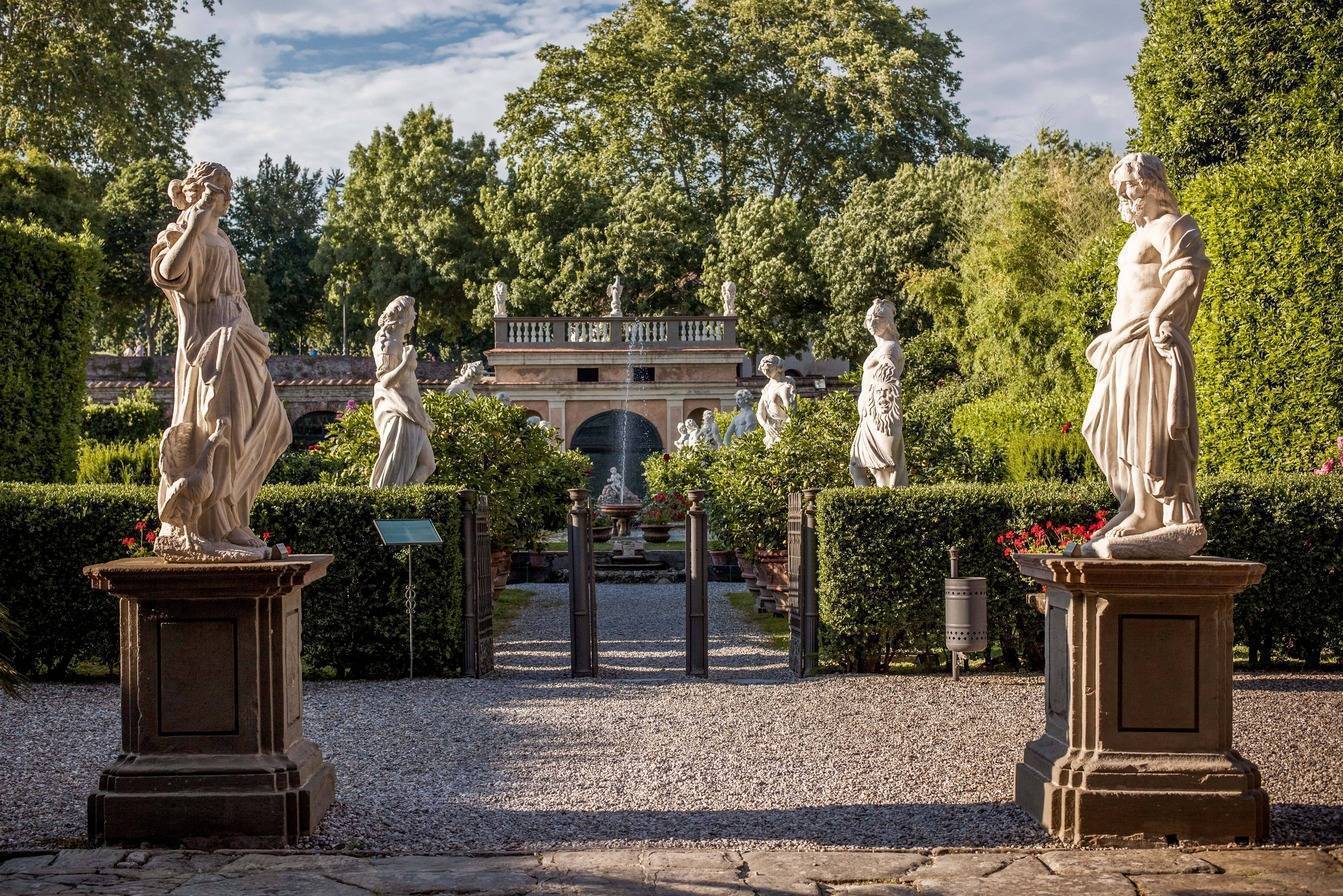 photo d'un jardin en italie avec des arbres, un bâtiment et une enfilade de statues